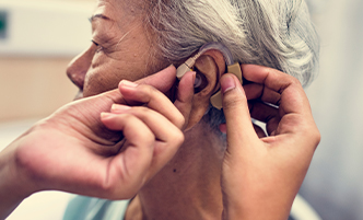 Hand placing hearing aid on woman
